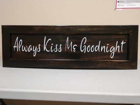 Dark brown, distressed wooden wall art with white lettering saying "Always Kiss Me Goodnight".