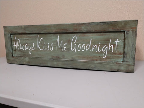 Green wooden gun concealment wall art with quote "Always Kiss Me Goodnight" leaning against wall.
