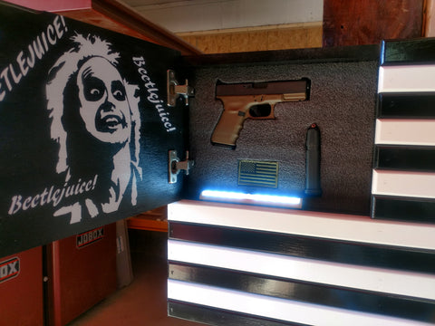 A black and white gun concealment flag, with Beetlejuice painted on the inside and motion activiated LED lights, with its hidden compartment open to reveal a handgun. 