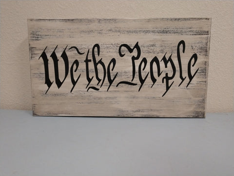 White, distressed gun concealment wall box with script "We The People" leaning against wall.
