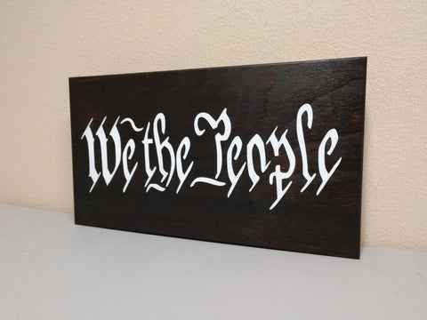 "We The People" black, wooden gun concealment wall decor leaning against wall.