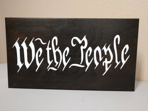 Black gun concealment wall decor with "We The People" in white script.