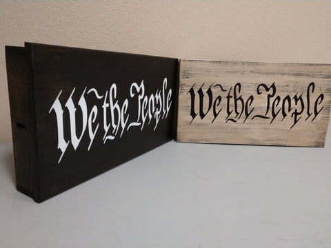 One black and one white, distressed wooden decor sign with "We The People" in script.