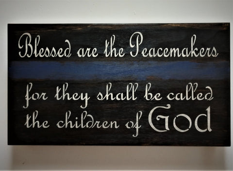 Black wall decor with blue stripe and white lettering saying "Blessed are the peacemakers for they shall be called the children of God".