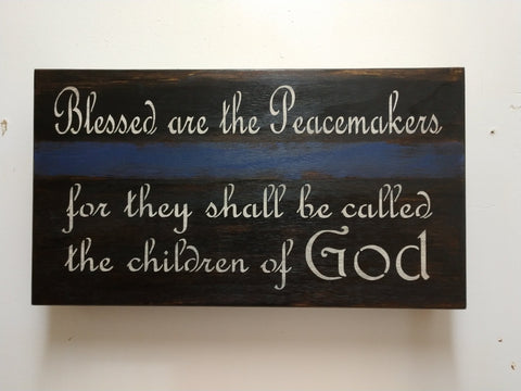 Dark brown, wooden wall decor with blue stripe and quote "Blessed are the peacemakers for they shall be called the children of God".