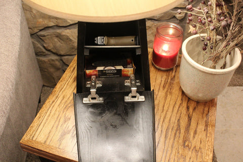 Looking down on a black wooden concealment lamp sitting on a side table with it's hidden compartment open revealing a handgun and a box of ammunition.
