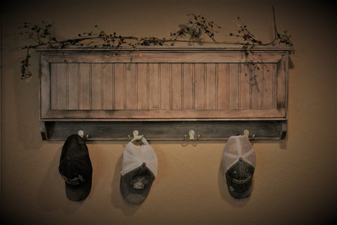 A gun concealment coat rack, made from wood and finished with a slate grey stain, with three hats hanging on it.