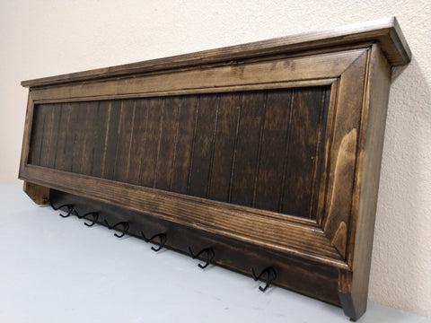 A gun concealment coat rack with six black metal hooks made from Walnut and finished with dark brown stain.