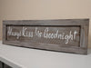 Light brown, distressed wall art with white lettering saying "Always Kiss Me Goodnight".