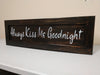 Dark brown, distressed wall art with white lettering saying "Always Kiss Me Goodnight".