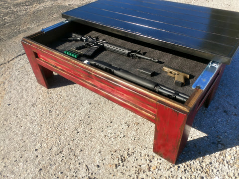 A sliding top gun concealment coffee table with a black painted top and red legs with it's top open to reveal a rifle and shotgun.