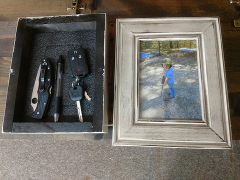 A 5x7 distressed white gun concealment picture frame, separated into two pieces, including its hidden compartment with a set of car keys, pocket knife and pen inside.