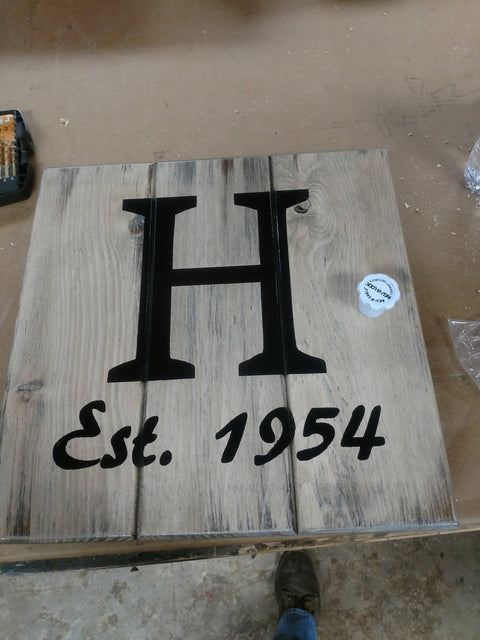 A white, distressed gun concealment sign, with the letter H and "est. 1954:" painted in black. 