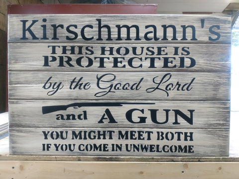 A white, distressed gun concealment sign, with the words "Kirschmann's this house is protected by the good Lord and a gun you might meet both if you come in unwelcome" painted in black. 
