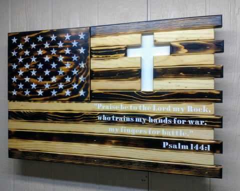 A gun concealment flag with a cross carved out of it and the words "Praise be to the Lord my rock, who trains my hands for war, my fingers for battle. Psalm 144:1" painted in white. 