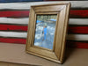 A 5x7 American wood gun concealment picture frame sitting in front of a red, white and blue concealment flag.