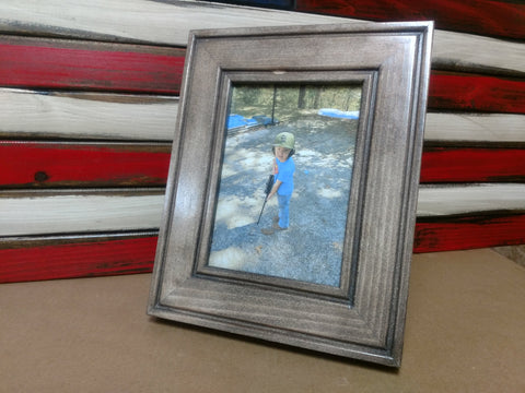 A 5x7 light grey gun concealment picture frame sitting in front of a red, white and blue concealment flag.
