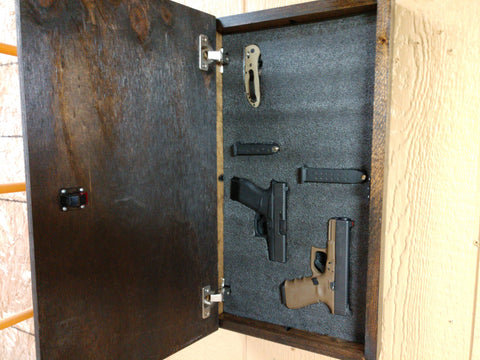 Interior of mini wooden wall art hanging on wall with 2 handguns, 2 ammunition pouches, and 1 knife held inside in foam.