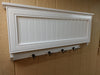 An angled view of a medium-sized wooden gun concealment coat rack, with four black metal hooks, painted white. 