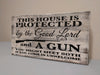 "This house is protected by the Good Lord and a gun" white, distressed gun concealment sign leaning against wall.