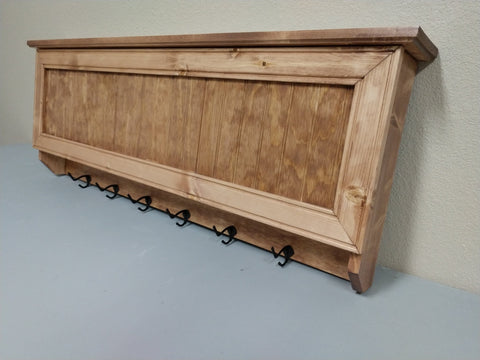 A gun concealment coat rack with six black metal hooks made from oak with a golden wood stain. 