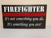 Hanging wood wall art with red stripe and lettering saying "Firefighter. It's not something you do. It's something you are!"