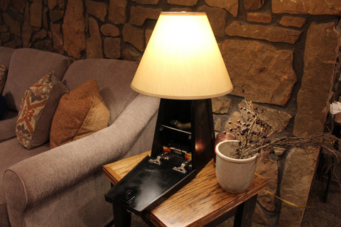 A black wooden gun concealment lamp, sitting on a side table with its hidden compartment open revealing a handgun. 