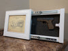 A white, 8x10 concealment picture frame with its hidden compartment open to reveal a handgun with a magazine. 