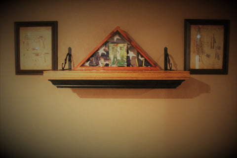 A wooden gun concealment wall mantle, hanging on a wall with folded American flag in a flag case sitting on top.