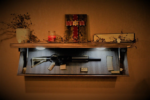 A light brown, wooden gun concealment shelf hanging on a wall with it's hidden compartment open revealing a semi-automatic rifle. 